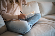 A woman sits on a couch writing in a journal, capturing a moment of relaxation and mindfulness, embodying WeNatal's focus on wellness and balance.